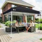 Tonnelle pliante 3x3 en place sur terrasse, famille assise autour d'une table sous l'abri noir, mobilier de jardin et maison en arrière-plan. Sono Médoc