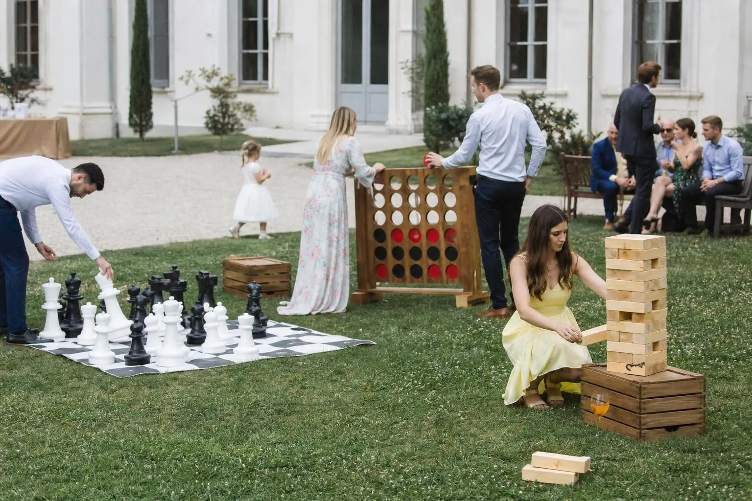 Jeu en plein air lors d’un mariage avec pièces d’échecs géantes et tour de Jenga géante, ambiance festive et invités en arrière-plan. animations originales pour un mariage