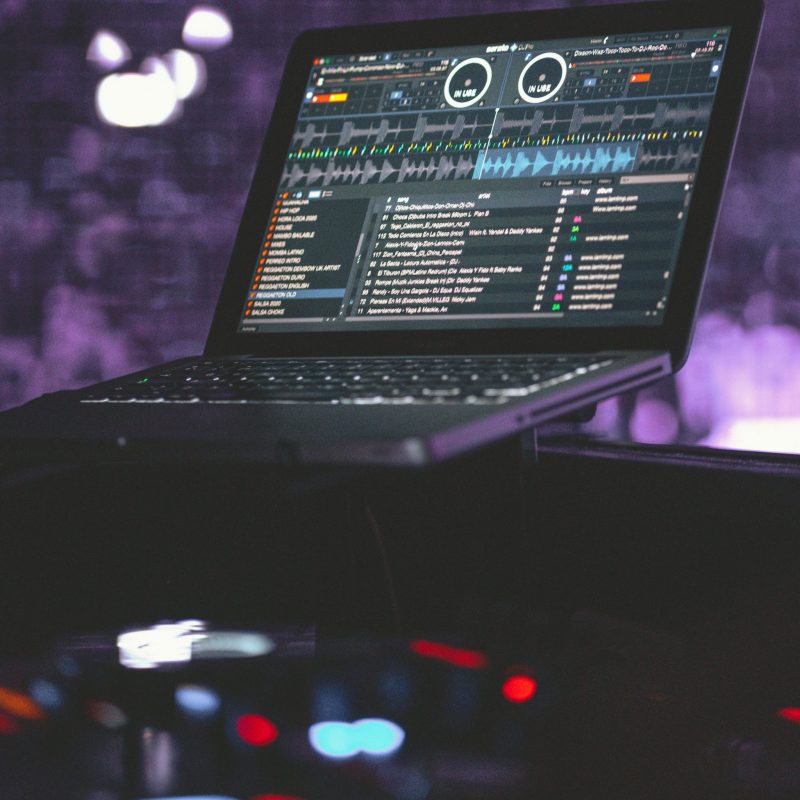 Écran d’ordinateur portable affichant une interface de logiciel DJ professional avec decks, onde sonore et liste de morceaux.