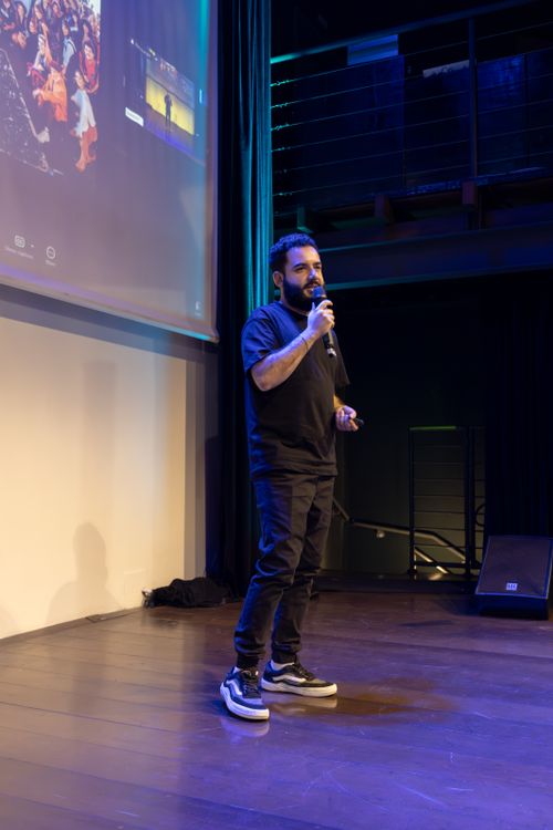 Homme sur scène, micro à la main, présente devant un grand écran projector dans une salle de conférence, ambiance acoustique adaptée. sonorisation salle de conférence comment choisir