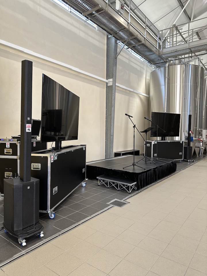 Équipement de sonorisation sur scène avec haut-parleurs, consoles et micros dans une salle de spectacle.