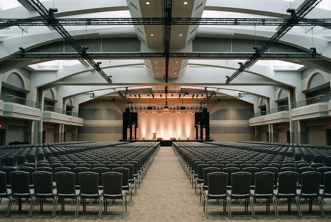 Salle de conférence grande capacité, scène éclairée et rangées de chaises professionnelles pour créneaux événementiels. agence événementielle Bordeaux.
