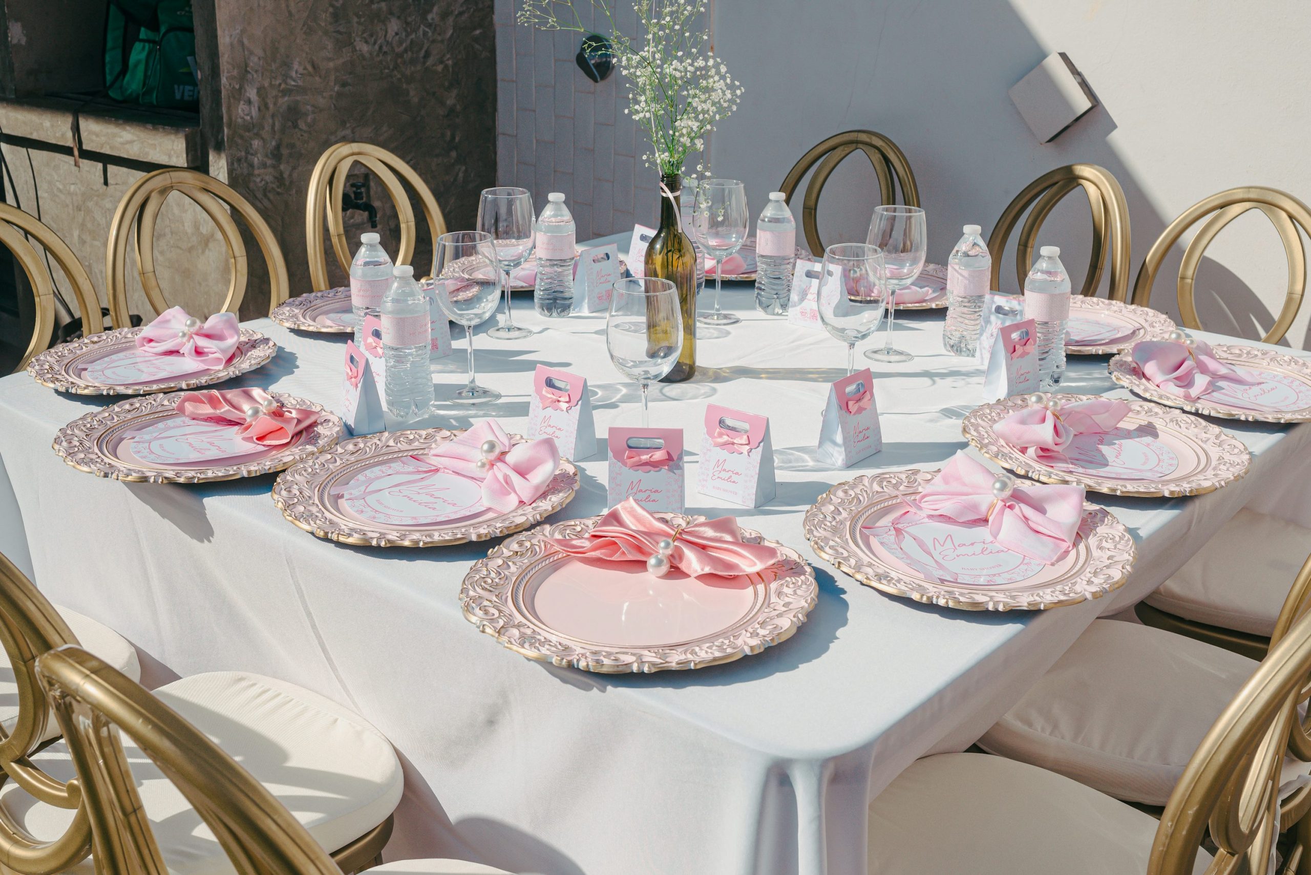 Table ronde dressée pour anniversaire avec vaisselle élégante, rubans roses et bouteilles d’eau; décor et matériel pour soirée d'anniversaire idoines.