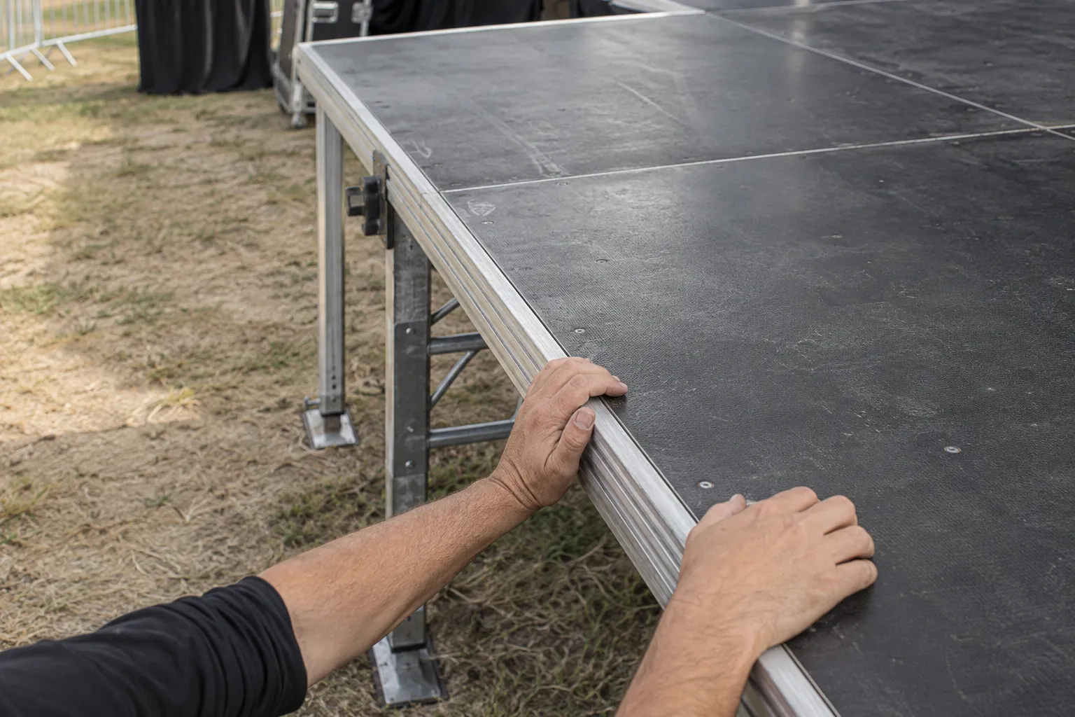 Deux mains saisissent le rebord d’une scène mobile en extérieur.