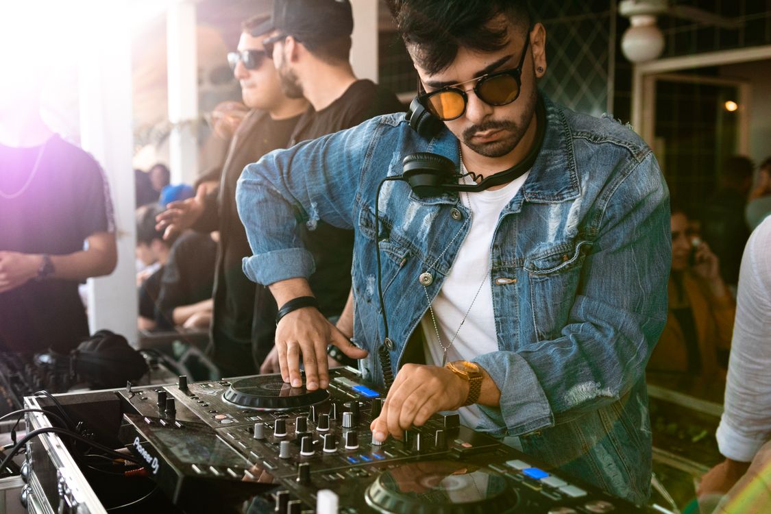DJ professionnel en train de mixer sur une platine avec casque autour du cou et lunettes de soleil.