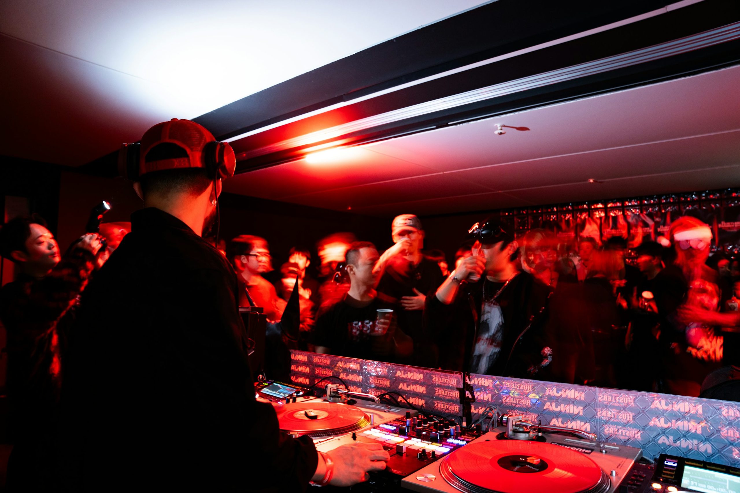 DJ en train de mixer devant une foule dans une arrière-plan sombre et lumineuse.