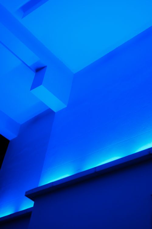 Éclairage bleu sur les murs et les rebords d’un bâtiment intérieur avec des lignes géométriques.