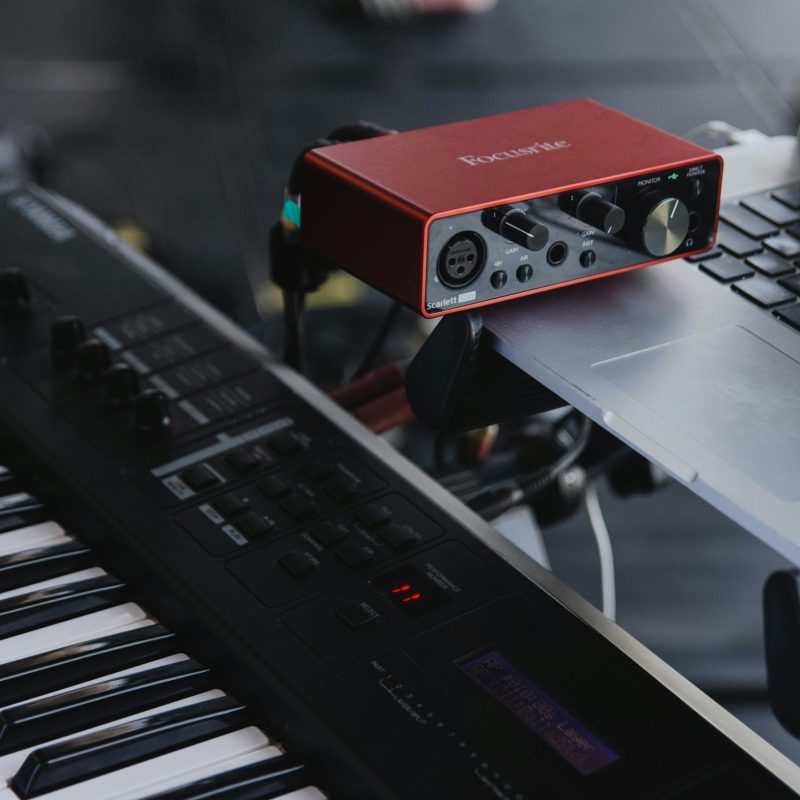 Interface audio rouge reliée à un ordinateur, posée au-dessus d’un clavier de synthétiseur noir.