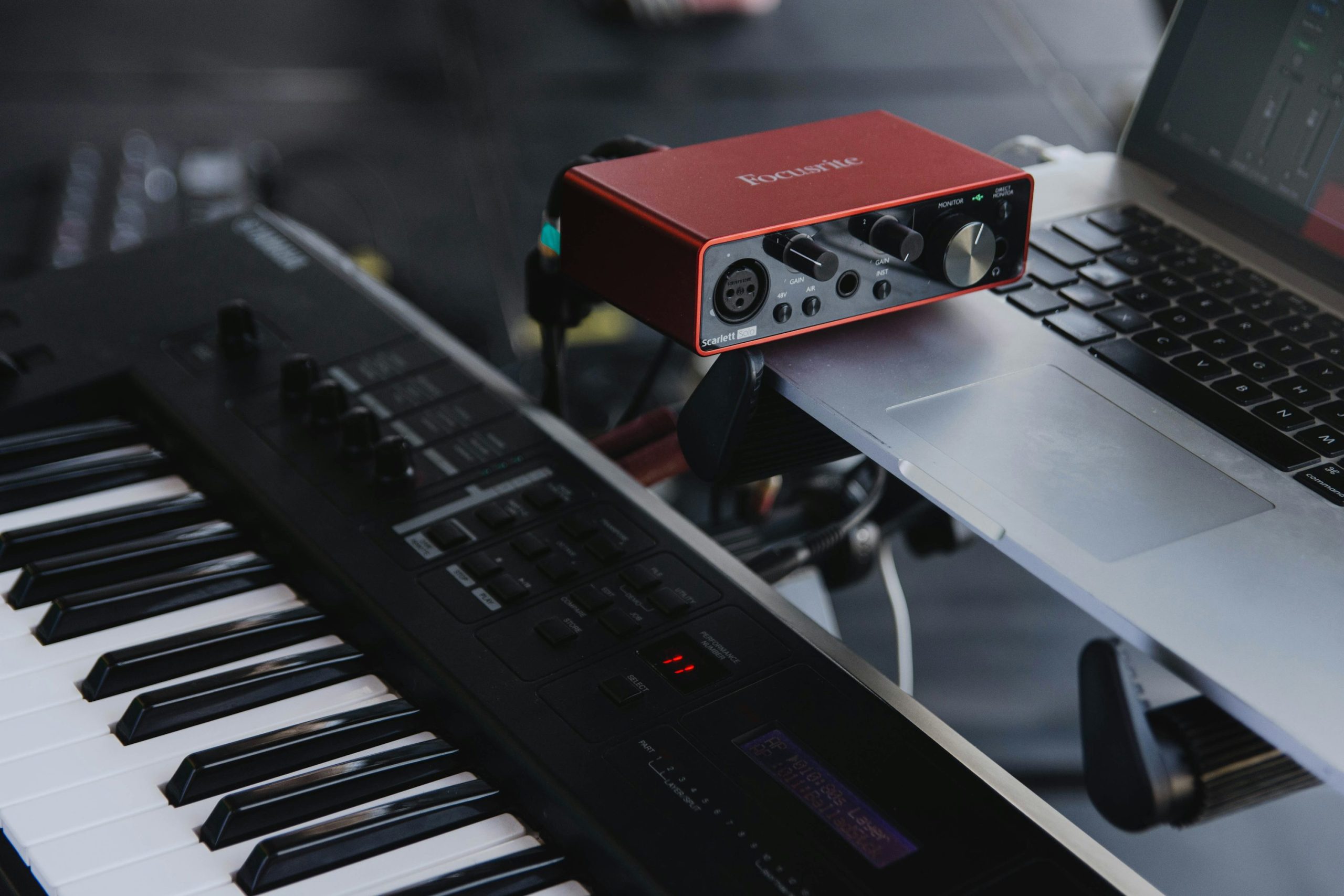 Interface audio rouge reliée à un ordinateur, posée au-dessus d’un clavier de synthétiseur noir.