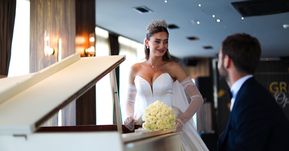 Mariée en robe blanche et diadème, debout au piano à queue, tenant bouquet de roses blanches et échangeant un sourire avec