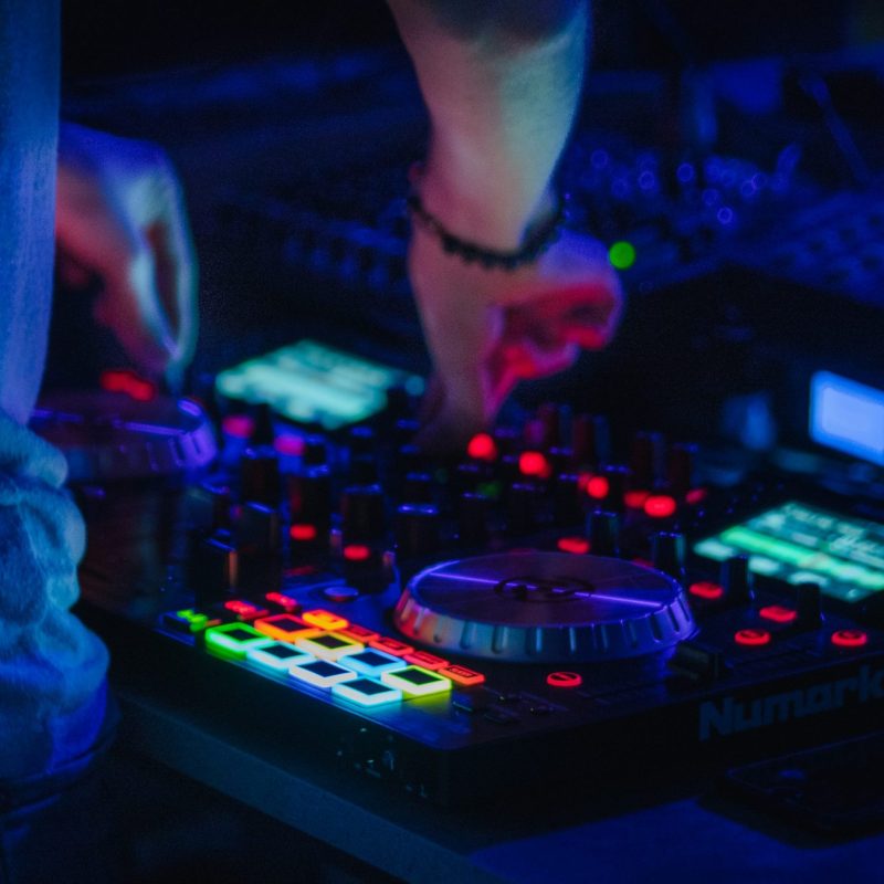 Ordinateur et contrôleurs de mixage audio avec voyants lumineux et boutons colorés en action sur une table de son.