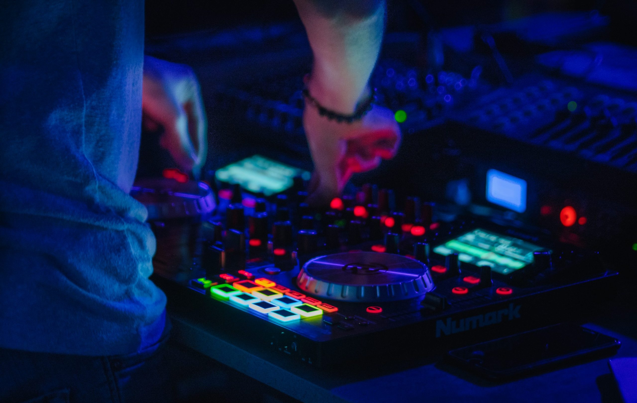 Ordinateur et contrôleurs de mixage audio avec voyants lumineux et boutons colorés en action sur une table de son.